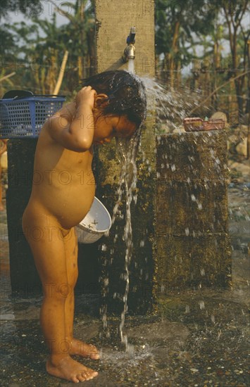 LAOS, Hygiene, Washing, Young Hmong girl washing under stand pipe in Hmong returnee villages for ex-refugees from Thailand.