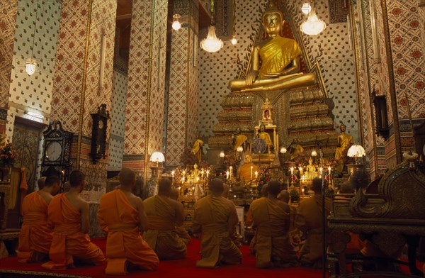 THAILAND, Bangkok, "Monks pray, kneeling down in front of large golden Buddha at Wat Arun. The Temple of Dawn."