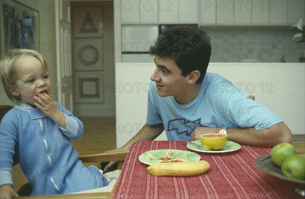 ENGLAND, London, Children, Male au pair with boy aged twenty months eating fruit for  breakfast.