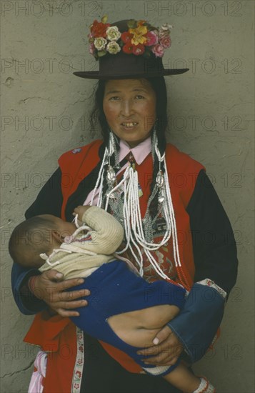 CHINA, Qinghai Province, Huzhu District, Tu minority Yellow Hat Buddhist woman carrying child wearing open backed trousers instead of nappy.