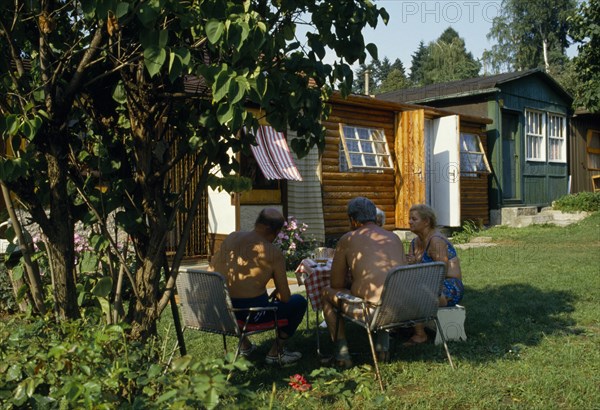 CZECH REPUBLIC, People, Cernosice Holiday Homes. Elderly couples sitting around a table on the grass outside wooden chalets.