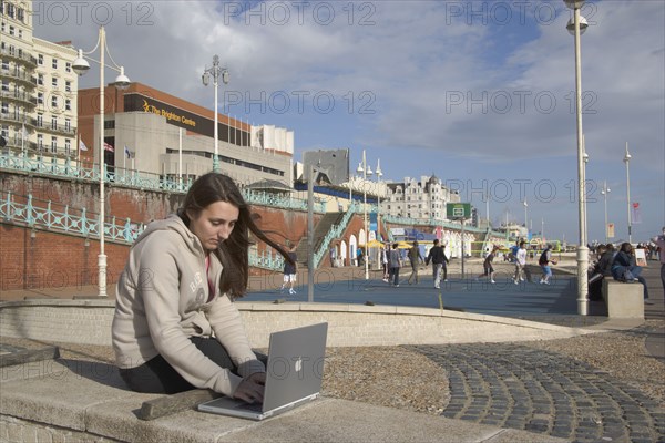 ENGLAND, East Sussex, Brighton, Woman using a laptop to surf the internet  in the free WiFi zone on the beach between the piers