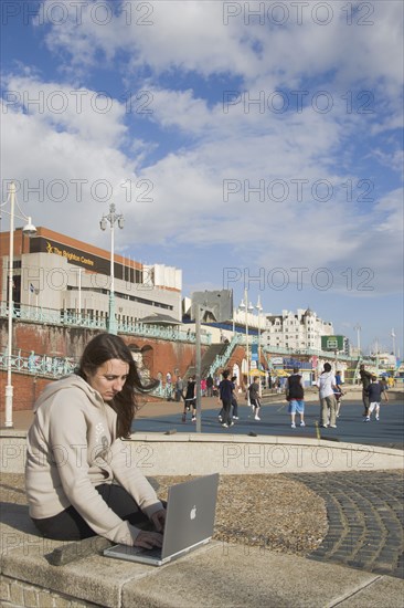 ENGLAND, East Sussex, Brighton, Woman using a laptop to surf the internet  in the free WiFi zone on the beach between the piers