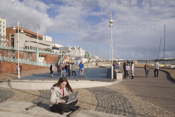 ENGLAND, East Sussex, Brighton, Woman using a laptop to surf the internet  in the free WiFi zone on the beach between the piers