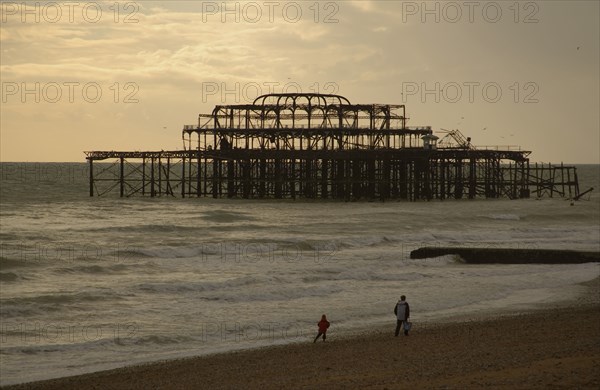 ENGLAND, East Sussex, Brighton, The ruined West Pier with a man and small child walking together along shoreline.