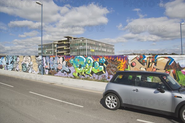 ENGLAND, East Sussex, Brighton, View across road with a Mini car traveling past towards a wall displaying colourful graffiti.