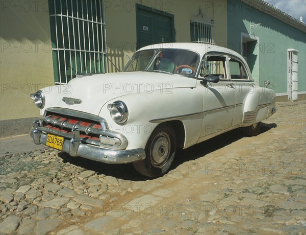 CUBA, Havana, Trinidad de Cuba, A white Chevy sits amidst the town’s features of cobblestone streets.