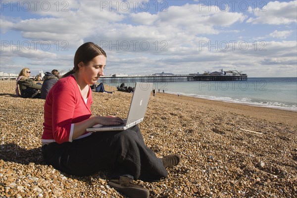 ENGLAND, East Sussex, Brighton, Woman using a laptop to surf the internet  in the free WiFi zone on the beach between the piers