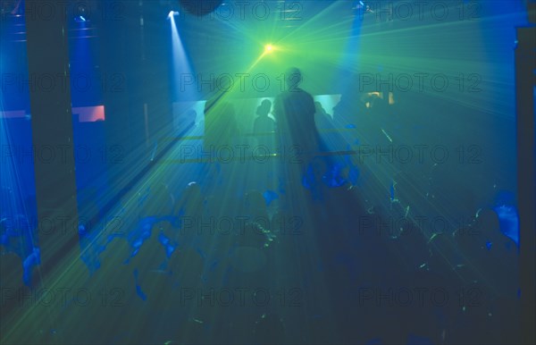 THAILAND, Bangkok, The Ministry of Sound night club. Two people on a platform above crowd of dancers. Blue and green lighting.