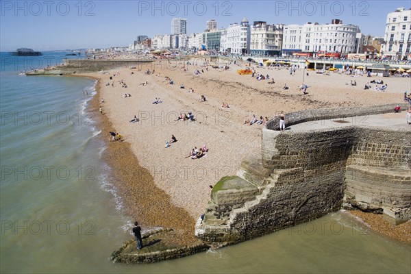 ENGLAND, East Sussex, Brighton, The beach and seafront with flint groyne in the foreground seen from Brighton Pier with the city in the distance