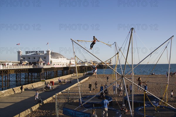 ENGLAND, East Sussex, Brighton, Brighton Pier and amusements on the beach with people  bouncing on trampolines whilst suspended from harnesses on elastic ropes