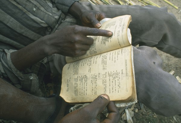 ANGOLA, Huambo, Kaala.  Displaced men living in disused factory practising reading skills with Portuguese grammer book.