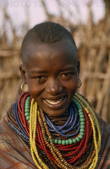 UGANDA, Karamoja District, Portrait of Karamojong woman wearing multiple coloured bead necklaces.  Her hair style indicates her clan.