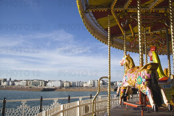 ENGLAND, East Sussex, Brighton, Empty fairground carrousel on Brighton Pier with the City and beach in the distance