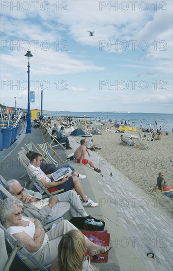 ENGLAND, Dorset, Bournemouth, People sat on deckchairs along seafront.