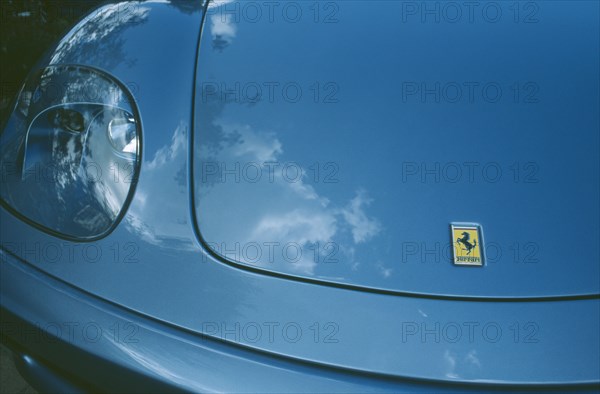 TRANSPORT, Road, Cars, Detail of blue Ferrari emblem and front light with clouds reflected in paintwork.