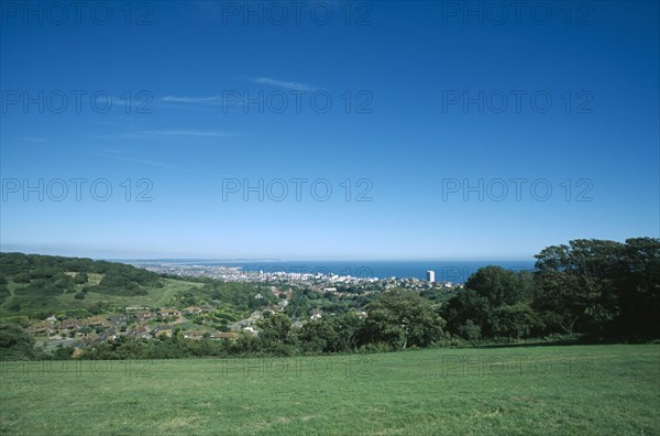 ENGLAND, East Sussex, Eastbourne, Elevated view from the South Downs over fields towards town and coastline.
