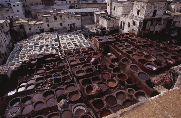 MOROCCO, Fes, Chouwara Tanneries.  Elevated view over the tanner’s pits with city buildings beyond.