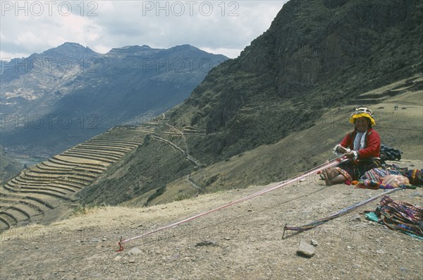 PERU, Cusco, Pisac, "Quechuan Indian woman weaving, inca terracing behind. Sacred Valley"