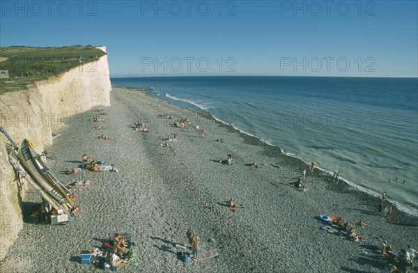 ENGLAND, East Sussex, Birling Gap, View over occupied peeble beach with boat leaning against cliff face.