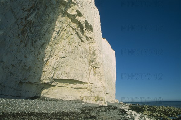 ENGLAND, East Sussex, Birling Gap, Base of cliff face partially in shadow with rockpools and pebble beach.