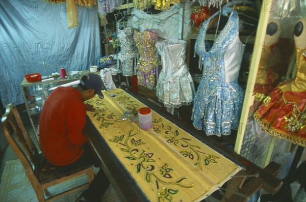 BOLIVIA, La Paz, Costume maker for Oruro Carnival. Man attaching sequins to material.