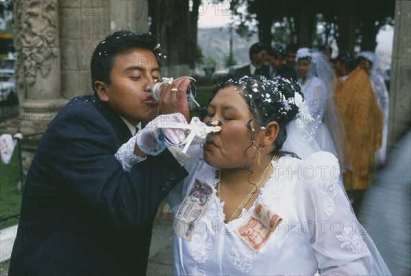 BOLIVIA, La Paz, Wedding in El Monticulo. Bride and Groom interlocking arms and drinking. Money attached to Bride’s dress.