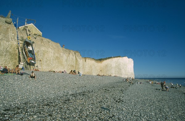 ENGLAND, East Sussex, Birling Gap, View across occupied peeble beach with boat leaning against a section of cliff face.