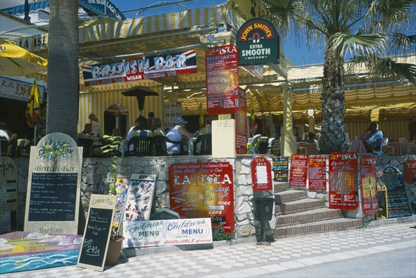 SPAIN, Andalucia, Benalmadena, Promenade with English restaurant and bar signs. People sat at tables.Costa del Sol