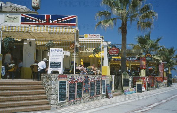 SPAIN, Andalucia, Benalmadena, Promenade with English restaurant and bar signs. People sat at tables.Costa del Sol