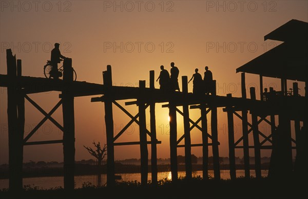MYANMAR, Amarapura, U Bein Bridge near Mandalay at sunset with silhouetted figures of monks and cyclist crossing.