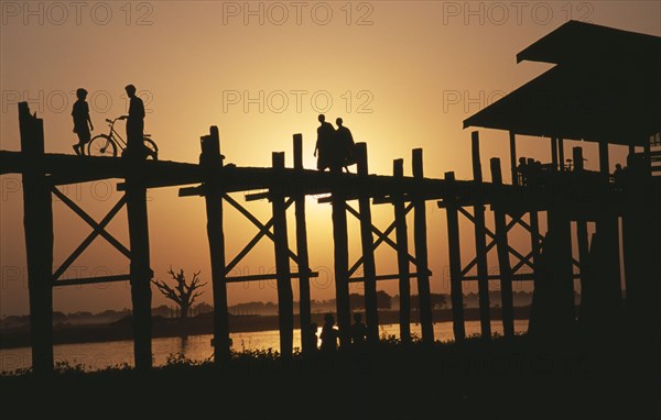 MYANMAR, Amarapura, "U Bein Bridge near Mandalay at sunset with silhouetted figures of monks, child and cyclist crossing."