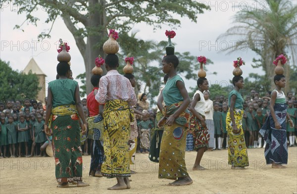 CONGO, Kimpese, Dancers at festival carrying gourds and bottles filled with flowers on their heads and watching crowd behind.