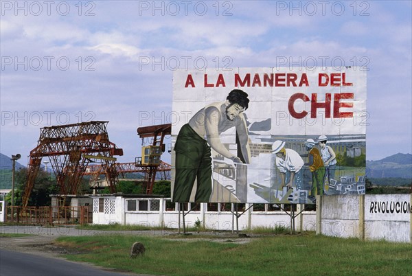 CUBA, Santiago de Cuba, "Billboard celebrating the work of Che Guevara, with industrial facilities behind."