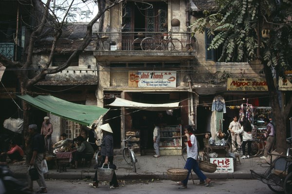 VIETNAM, North, Hanoi, "City Old Quarter street scene with roadside vendors, pedestrians and bicycle on balcony of delapidated old colonial building above."