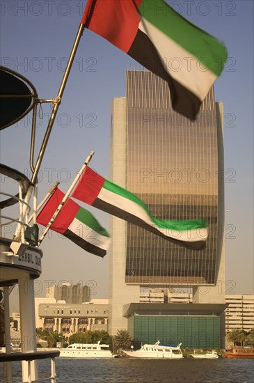 UAE, Dubai, The National Bank with Emirates national flags flying from the stern of a boat in the foreground.