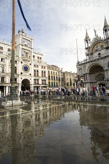 ITALY, Veneto, Venice, Aqua Alta High Water flooding in St Marks Square with tourists on elevated walkways above the flooded piazza beside St Marks Basilica and the Torre dell'Orologio clock tower