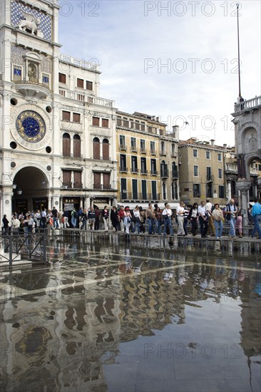 ITALY, Veneto, Venice, Aqua Alta High Water flooding in St Marks Square with tourists on elevated walkways above the flooded piazza beside St Marks Basilica and the Torre dell'Orologio clock tower