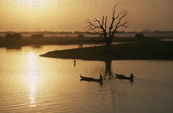 MYANMAR, Taungthaman Lake, View from U Bein Bridge at Amarapura near Mandalay with canoes silhouetted against water reflecting golden sunset and trees and landscape in drifts of mist.