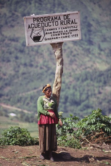 GUATEMALA, Huehuetenango, "Indigenous woman standing below a sign describing a village water project, highlands."