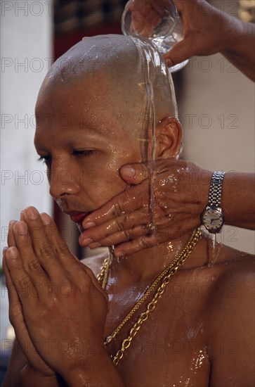THAILAND, Bangkok, Novice monk having water poured over newly shaved head during ordination ceremony.