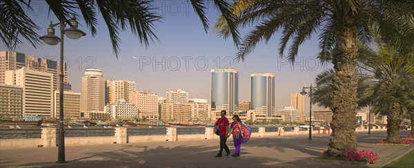 UAE, Dubai, View of Deira across Dubai Creek from Bur Dubai. A couple holding hands and palm trees in the foreground.