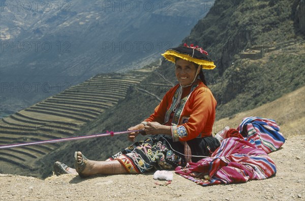 PERU, Cusco, Pisac, "Quechuan Indian woman weaving, inca terracing behind. Sacred Valley"