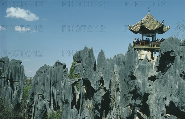 CHINA, Yunnan Province, Shilin, The Stone Forest. Grey limestone rock pinnacles with tourists viewing from under a small traditional roof.