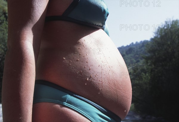 SPAIN, Pregnancy, Pregnant woman in a bikini with water droplets on tummy.