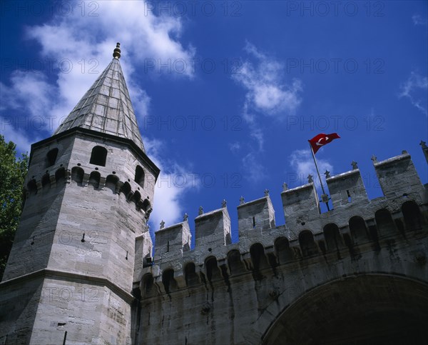 TURKEY, Istanbul, "Topkapi Palace. Entrance to grounds looking up at a tower, crenelated wall and Turkish flag flying."