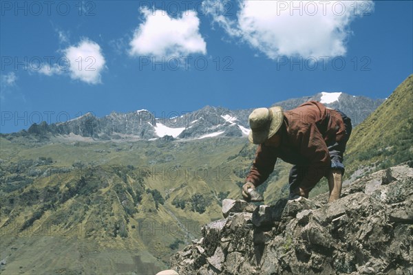 PERU, Cusco, Cancha Cancha, "Local Quechuan man building a house, mountains in the distance."