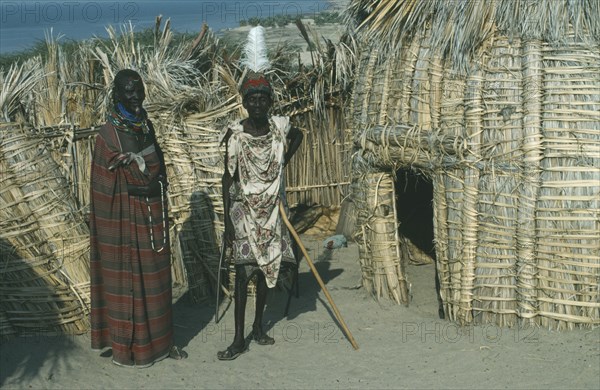 KENYA, Lake Turkana, "Turkana tribe, two men standing outside a traditional hut made from dry fan palm leaves."