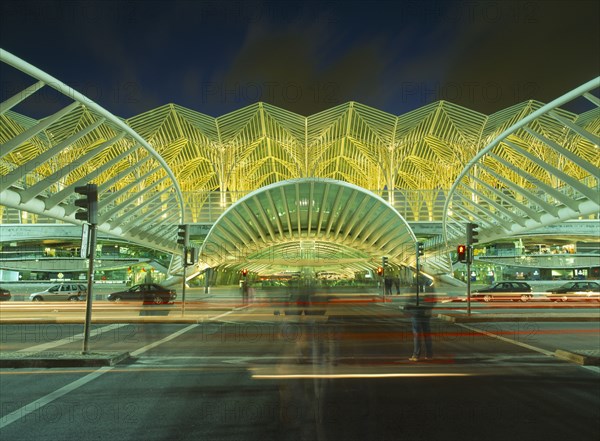 PORTUGAL, Lisbon, Exterior of bus station on the Expo site illuminated at night with light trails from passing traffic and people in blurred movement in foreground.