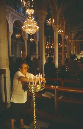 GREECE, Cyclades Islands, Syros, Ermoupolis. The interior of the Catholic Church of Ag. Yiorgios. Candles being lit and people stood at the pews